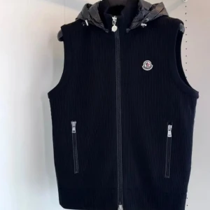 Svart Moncler dunväst med huva - Marinblå dunväst från Moncler med ribbad struktur och glansig huva. Västen har två fickor med dragkedja och Moncler-logga på bröstet. Perfekt för lager-på-lager och snygg till streetwear. Stängs med dragkedja framtill.