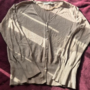 Beige kofta med v-ringning och knappar - Snygg beige kofta från InWear med v-ringad hals och knäppning framtill. Långärmad modell med diskret prickigt mönster i tyget. Tillverkad i mjuk viskosblandning med nylon för extra komfort. Perfekt att slänga över en t-shirt eller linne. Saknar en knapp men finns en extra som är lätt att sy dit. 