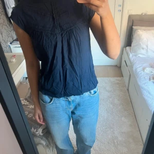 Mörkblå blus med korta ärmar - Säljer en mörkblå blus med korta ärmar och rund hals. Toppen har en lös passform och fina söm-detaljer upptill som ger en cool look. Perfekt att matcha med jeans eller kjol för en chill stil. Materialet känns lätt och luftigt.