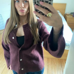 Mysig vinröd kofta med knappar - Säljer en fluffig och mjuk vinröd kofta med stora silvriga knappar framtill. Koftan har lång ärm och är stickad i ett skönt material som passar perfekt när det är lite kyligt. Enkel och stilren design som är lätt att matcha med jeans eller kjol.