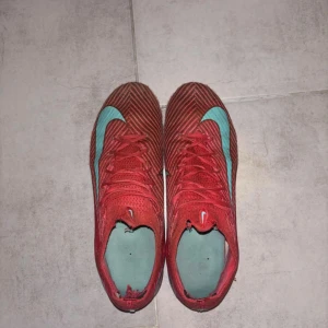 Nike Mercurial rosa fotbollsskor - Säljer ett par Nike Mercurial fotbollsskor i en snygg rosa färg med turkosa detaljer och snörning. Skorna har en låg profil och är tillverkade i syntetmaterial för bästa känsla på planen. Perfekta för dig som vill sticka ut med stil på fotbollsplanen. Men är använd då en hel säsong, och om ni vill ha bilder efter jag har tvättat dem så kan ni bara skriva till mig privat!