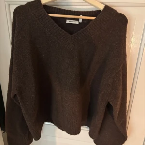 Brun stickad tröja från Weekday - Mysig brun stickad tröja från Weekday med v-ringad hals och breda muddar. Tröjan har en loose passform och är perfekt för kyligare dagar. Enkel att matcha med både jeans och kjol.