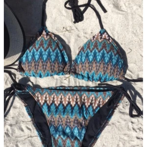 Mönstrad trekantsbikini med knyt - Säljer en snygg trekantsbikini med blått, brunt och svart mönster. Både överdel och underdel har knyt i sidorna och nacken för justerbar passform. Bikinin har ett coolt grafiskt mönster och tunna svarta band. Ganska liten storlek så skulle säga S, men köpt M. Perfekt för stranden eller poolen! 