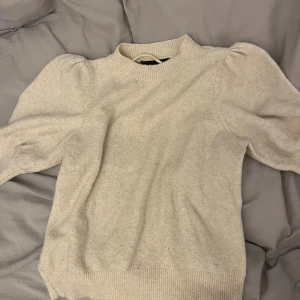 Beige stickad tröja med puffärm - Beige stickad tröja med rund hals och ribbade muddar. Tröjan har puffärmar som ger en cool och trendig siluett. Perfekt för dig som gillar en enkel men ändå snygg look. Mjuk och skön kvalitet som passar till många olika stilar. Möjligtvis lite nopprig men fortfarande väldigt mjuk och knappt använd! 