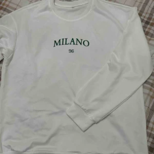 Vit sweatshirt Milano 96 tryck - Vit sweatshirt med grönt Milano 96-tryck på bröstet. Tröjan har rund hals, långa ärmar och ribbade muddar vid ärmslut och nederkant. Ganska tunt tyg så du vet💕