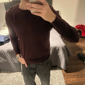 Vinröd stickad tröja med rund hals - Snygg vinröd stickad tröja med rund hals och långa ärmar. Tröjan har en enkel och stilren design utan mönster eller detaljer, perfekt att matcha med jeans eller chinos. Mjuk och skön känsla, passar dig som gillar klassisk stil.