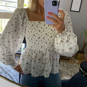 Blommig blus från NA-KD - Blommig blus från NA-KD. Tyget är i linneblandning. Vit med rosa/lila blommor. Aldrig använd. Storlek 42.