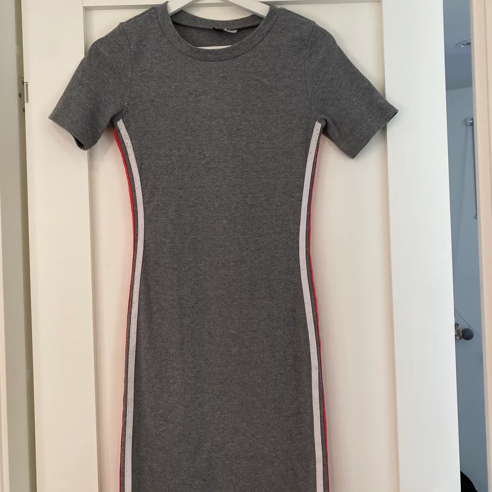 Grå klänning med vita & röda ränder på sidorna från H&M,  stl M i använt skick. Klänningen går till lite ovanför knäna. (säljes för 60kr +  frakt). Klänningar.
