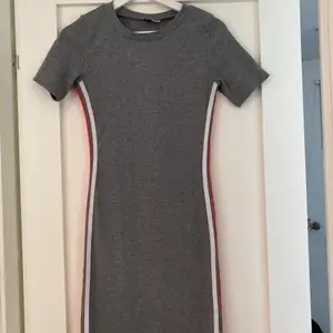 Grå klänning med vita & röda ränder på sidorna från H&M,  stl M i använt skick. Klänningen går till lite ovanför knäna. (säljes för 60kr +  frakt)