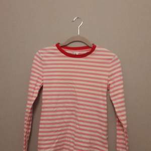 En långärmad tröja med rosa och vita ränder och en röd krage säljs i stlm 