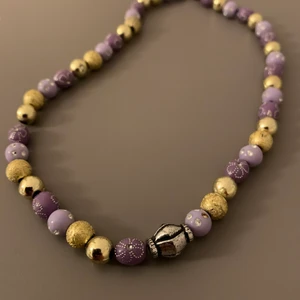 Lila och guldigt halsband - Fint halsband i lila och guld. Egengjort och aldrig använt. Köpare står för frakt.