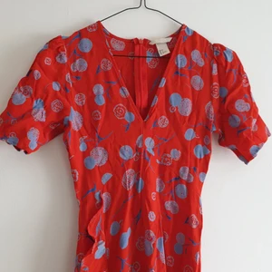 Blommig klänning H&M storlek 34 - Blommig sommarklänning i rött och blått med djupare urringning. Dragkedja i ryggen och volang på kjolen.