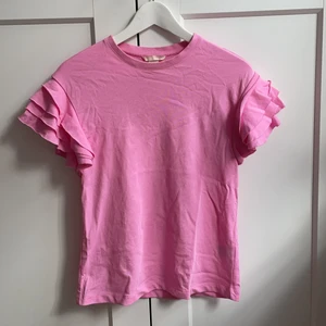 Rosa t-shirt från H&M - Säljer denna rosa t-shirt från H&M. Superfina volangdetaljer på ärmarna!! Den är använd ett fåtal ggr och är i fint skick. Priset är exklusive frakt