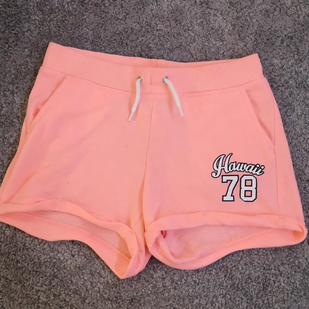 Neon rosa mjukis shorts med texten Hawaii 78 på högra låret. Väldigt stretchiga och mjuka med resor i midjan och snörning där framme. I väldigt fint skick med 2 fickor. Storlek:158. Shorts.