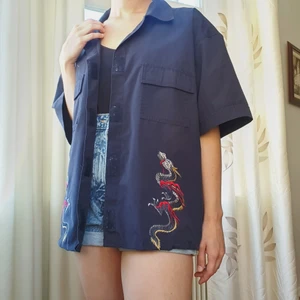 Blå skjorta med drakar - Riktigt najs mörkblå skjorta med drakar. Har klippt av den då den var för lång för mig och sytt in kanten själv. Stygnen är inte speciellt snygga men på långt håll märks de inte, och vill man går de alltid att göra om själv :-)   På baksidan har den typ lite flame mönster (skriv för fler bilder) och det finns en fläck ovanför ena bröstfickan (bild 3). Skriv om du har fler frågor.