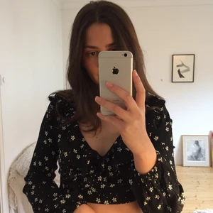 Kort blommig topp - En svart långärmad kort topp med blommor. Relativt tunt tyg som inte är strechigt. Volanger vid urringningen och resor i slutet på ärmarna. Aldrig använd. Ska vara strl 38 men är mer en 34/36.