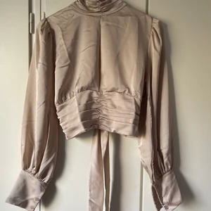 Topp med öppen rygg   - Topp med tre knappar runt hals med en liten öppning vid byst som är relativt diskret. Öppen rygg men knytning kring nedre delen av ryggen, se bild 2.   Helt oanvänd, tagg finns kvar på plagget. Frakt tillkommer. 