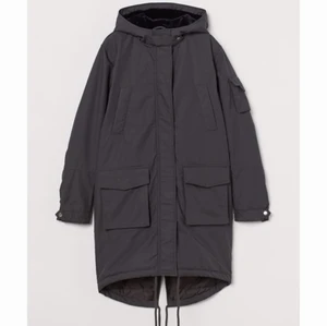 Mörkgrå Jacka - En parkas med pilefodrad huva. Parkasen har hög krage med slejf och trycknapp samt dold dragkedja fram. Handvärmarfickor upptill och utanpåfickor fram med lock och kardborreknäppning samt öppning i sidorna. Ärmar med slejf och tryckknapp nedtill varav en ärm med ficka och lock samt kardborreknäppning. Dragsko i nederkant och slits bak.  Storleken är 44 och den är i nyskick  NYPRIS 699:-