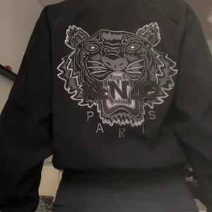 Kenzo jacka - En kenzo jacka med ett stort broderat ”kenzolejon” på ryggen. Stora muddar vid armarna och vid slutet av jackan. Köpt i köpenhamn för 4 år sedan men har inte använt den tillräckligt för att kunna ha kvar den. Den ser knappt använd ut, lappen där storleken står håller på att lossna, annars inga märken. Inköpspris 5000kr. 