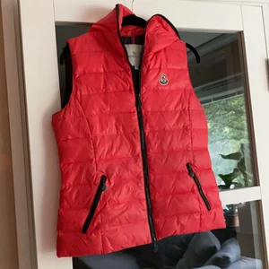 Monclerväst strl S/M - Monclerväst med dragkedja. Går att dra upp längst med hela luvan. Har några år på nacken men absolut i gott skick. Storlek 3, skulle säga att den passar S/M beroende på kroppsform och hur man vill att den ska sitta. 