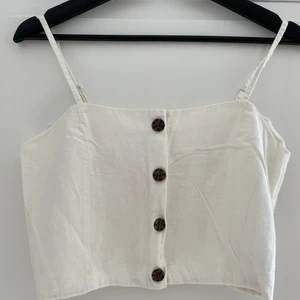 Vitt linne med knappar - Vitt linne med knappar i linneblandat material. Fyra knappar + en extra. Går att reglera axelbanden. Storlek 38