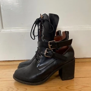 Jeffrey Cambell boots - Mattsvarta boots i läder från Jeffrey Campbell med omlottspännen och hög plös med snörning, dragkedja bak. Jättesköna att gå i. Robusta sulor med mycket lite slitage, och märken på klackarnas insida då jag cyklade med dem en gång. (Se bild)  Köpte 2014 i USA och använda kanske fyra gånger sedan dess så dags att de får en ny ägare! Amerikansk storlek 7.