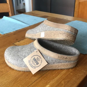 Haflinger - Grizzly Torben innerofflor  - Cremefärgade ulltofflor i stl 41 med oöverträffad passform. De absorberar fukt, håller värme och omger hela foten! Innersulan är gjord av filt med en förformad fotbädd. Och under, en slitstark korksula med halkskydd av naturligt latex. Perfeka nu när kylan smyger sig på! Levereras oanvända i orginalförpackning. 