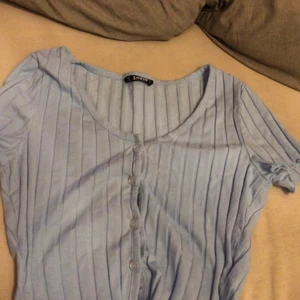 Blåa topp - En fin blå t-shirt med ”ränder”. Man kan ha den öppen men också stängd. Sitter fint. Och slutar ungefär vid naveln. Den är stretchig. 