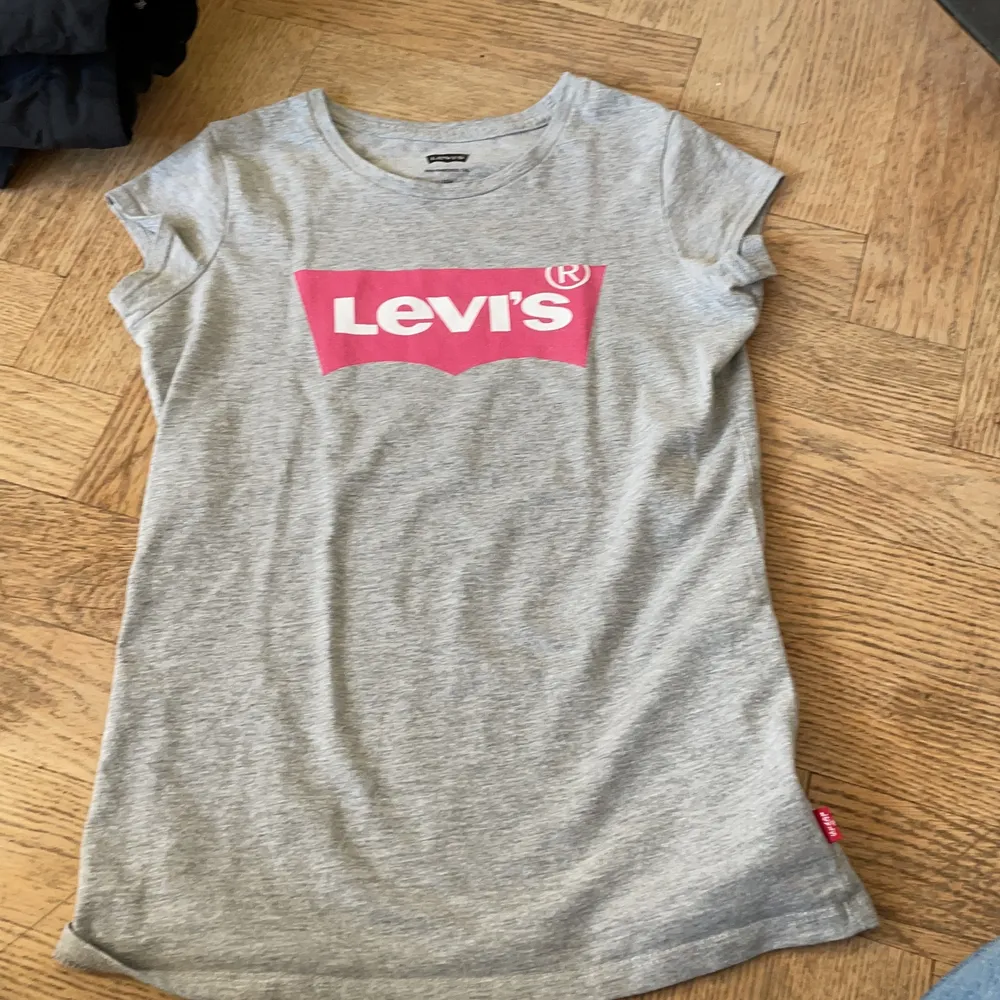 En grå tröja med ett tryck med märket Levis och med rosa färg!. T-shirts.