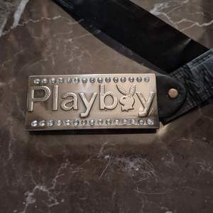Ett svart skärp med playboy märket. 97 cm långt skärp, 3.7 cm brett. Playboyloggan är 11 cm lång och 4.8 cm bred.