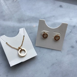 Guldiga örhängen och halsband - Populära och fina guldiga små örgängen och ett matchande halsband med en liten berlock. Oanvända och köpta på glitter💕köparen står för frakt!