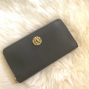 DKNY plånbok - Plånbok från DKNY. Köpt för 1200 på Åhléns. Grå med guld detaljer. 8 fack för kort samt 3 fack för kontanter, en med dragkedja för mynt i mitten. Finns att hämta i Alby eller kan mötas upp i Stockholms området. Kan skickas i posten också (köparen står för frakten)