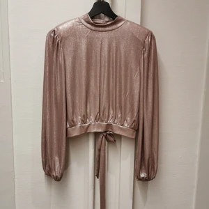 Metallictopp med öppenrygg - Supersnygg metallic rosa partytopp med öppen rygg, axelvadd och rosett på baksidan. Designprov, bara en finns. 