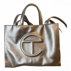 Telfar väska ! - Från det populära märket Telfar. I gott skick från Vestire Collective. I den mest underbara silvriga färgern! Den har långa och korta handtag och kommer med den originella dustbagen. I medium-size, måtten är - djup : 13 cm, bredd: 38 cm och höjd: 28cm. Möts helst upp i sthlm annars exklusive spårbarfrakt. Kan gå ner i pris vid snabb affär !!! (Säljs pga att den ej har kommit till användning för det priset jag gett för den)