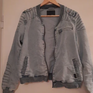 JACKA - Fejk jeans jacka, med luva. Luvan kan ta av och på. Luvan är grå. Fickan på bröstet är fejk.