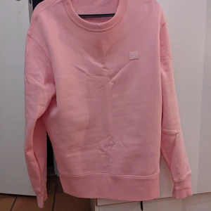 Acne sweatshirt face pale  - Väldigt fin tröja från Acne Studios, modell 'Fairview Face', färg Pale Pink, en fin korallrosa färg som verkligen sticker ut! Tröjan är rak i modellen. Endast använd vid 2 tillfällen och tvättad i fintvätt inför försäljning.  Material: 100% Bomull  Armhåla till armhåla: 55cm Midjemått: 51 cm Plaggets mått: 67 cm Ärmlängd: 64 cm