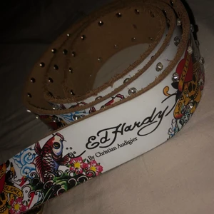 Ed Hardy bälte - Fint vintage bälte från Ed Hardy! 🤩                           Tagit två egna hål i den då bältet var för stort för mig,  för övrigt i okej skick, två av de små stenarna är lite slitna men det är inget man riktigt märker när man har den på :) skriv för fler bilder💕                                                                                      
