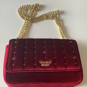 Victorias Secret väska - Liten väska från Victorias Secret. Väskan skiftar i lite cerise och mörkröd. Finns ett innerfack och ett fack på baksidan. Bandet går att justera så man har väskan i typ midjehöjd eller mer vid rumpan.  Aldrig använd. Köparen står för frakten🌸