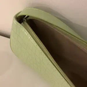 En grön baguetteväska som tyvärr inte kommer till användning längre. Den har en ljusgrön färg och silver detaljer. Väskan är i bra skick då den köptes i somras och inte är använd så mycket. Köptes för 73kr. Den har inga fack i sig.