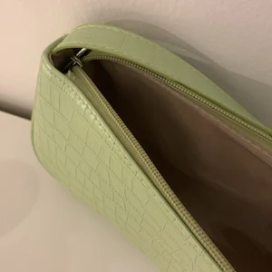 Grön baguetteväska  - En grön baguetteväska som tyvärr inte kommer till användning längre. Den har en ljusgrön färg och silver detaljer. Väskan är i bra skick då den köptes i somras och inte är använd så mycket. Köptes för 73kr. Den har inga fack i sig.