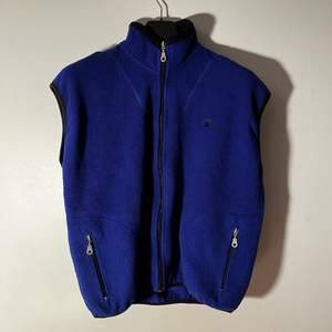 Blå Champion Fleece-Väst i fint skick, dock kan man hitta några små knottror lite här och där. Storleken går inte att se då etiketter missfärgats men skulle uppskatta en M/L för män. Midjebredden över fickorna när den ligger platt är 58cm. Fraktas spårbart med postnord, kan skickad med andra företag vid förfrågan.