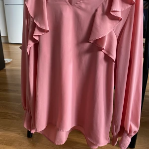 Blus  - Rosa blus med volanger och ”puffiga” ärmar. 