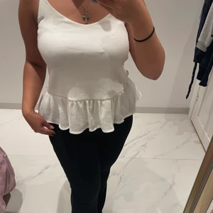 Blus  - Vit blus med smala axelband och volang längst ner.