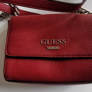 Guess röd liten axelväska  - Köpt på en finlandsfärja för flera år sedan, har varit väl använd och en av mina absolut favorit väskor! Vackert röd färg och utmärkt storlek för att få plats med det allra nödvändigaste i ett kompakt format.  Har en liten ytlig reva nedanför öppningsanordningen som enbart kan anas när väskan är öppen. Är annars i mycket gott skick. Har ett större fack med dragkedja på samt tre mindre som är direkt inpå varandra. Reglerbar axelrem.   Storlek: höjd 14 cm, bredd ca 20 cm och djup på ca 5.5 cm.  Köpare står för frakt. DM vid frågor eller intresse.