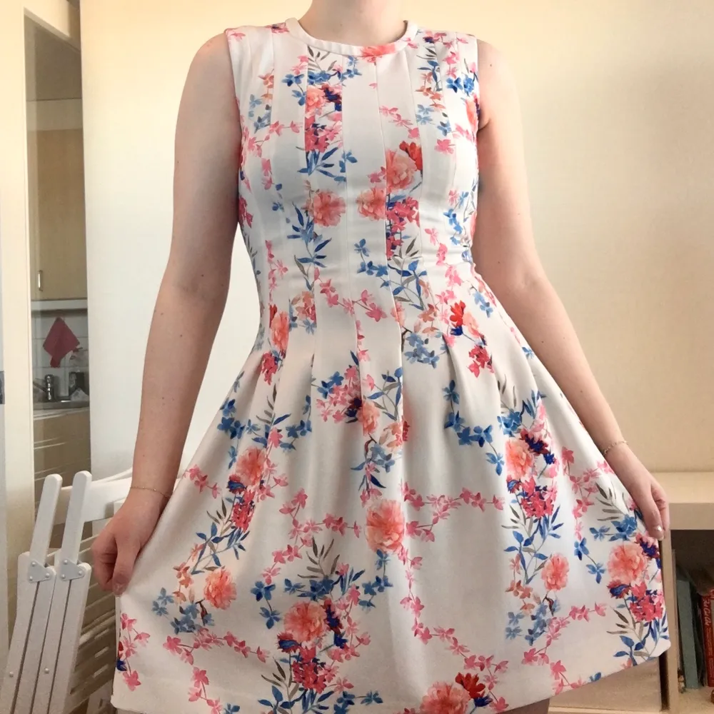 Size 38 dress with length from neck down 88cm. The waist is fitted around ~82cm but should work a few centimetres less as well. Condition is used but is still good quality! The dress has a little stretch in it and is white with Pink, Orange and Blue flowers. The back has a hidden zipper which goes down the back. . Klänningar.
