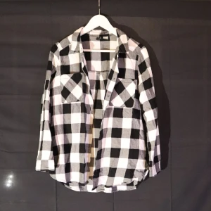 Svartvit rutig skjorta - Snygg svartvit rutig skjorta med långa ärmar och klassisk krage. Perfekt för en avslappnad stil. Skjortan har knappar framtill och två bröstfickor. Dam stl 40