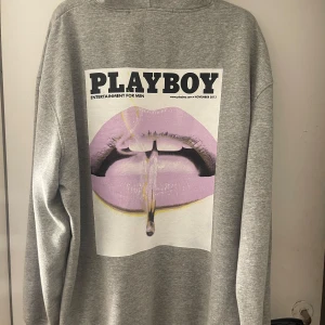 Grå hoodie med Playboy-tryck - Säljer en grå oversized hoodie med ett stort Playboy-tryck på baksidan och en liten logga på framsidan. Tröjan har en klassisk känguruficka och långa ärmar. Köpare står för frakt.