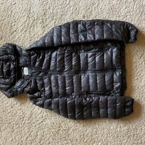 Svart dunjacka från McKinley - Säljer en svart dunjacka från McKinley med huva och dragkedja. Jackan är quiltad och perfekt för kyligare väder. Den har en stilren design och är lätt att matcha med olika outfits.