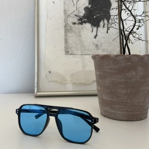 Svarta solglasögon med blå linser - Snygga svarta solglasögon med blå tonade linser. De har en modern design med en dubbel brygga och rektangulära glas. Perfekta för en cool look i solen!