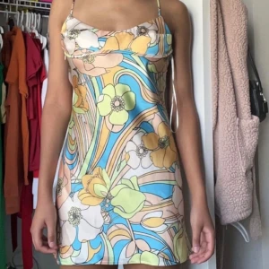 Färgglad blommig klänning med smala axelband - Lånade bilder! Säljer en superfin klänning med ett färgglatt blommönster i blått, gult och grönt. Klänningen har smala axelband och en kort längd, perfekt för sommarens varma dagar. Den har en lätt och luftig passform som gör den bekväm att bära.